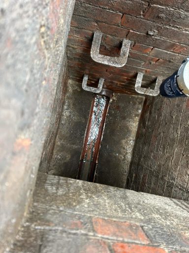 View down a narrow brick-lined well with metal hooks and water at the bottom.