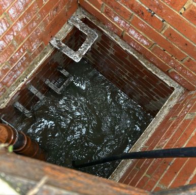 A deep, brick-lined well with water at the bottom and a pipe leading down.
