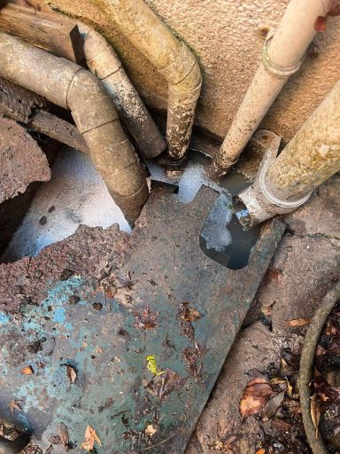 Pipes with water leak on a weathered surface with leaves scattered around.